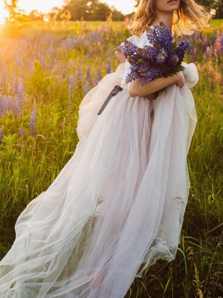 mariée dans un champ, avec une brassée de fleurs dans les bras